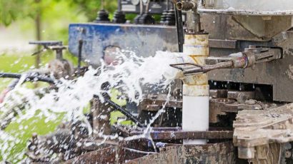 A drilling machine is actively jetting water or fluid, creating a spray as part of the drilling process.