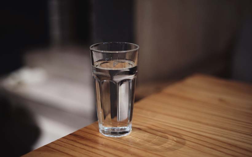 A clear glass filled with water is placed on a wooden table, set against a softly lit background.