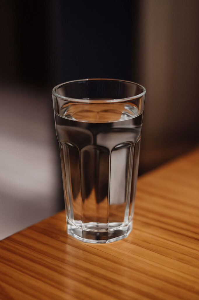 A clear glass filled with fresh water sits on a wooden table, emphasizing purity and hydration.